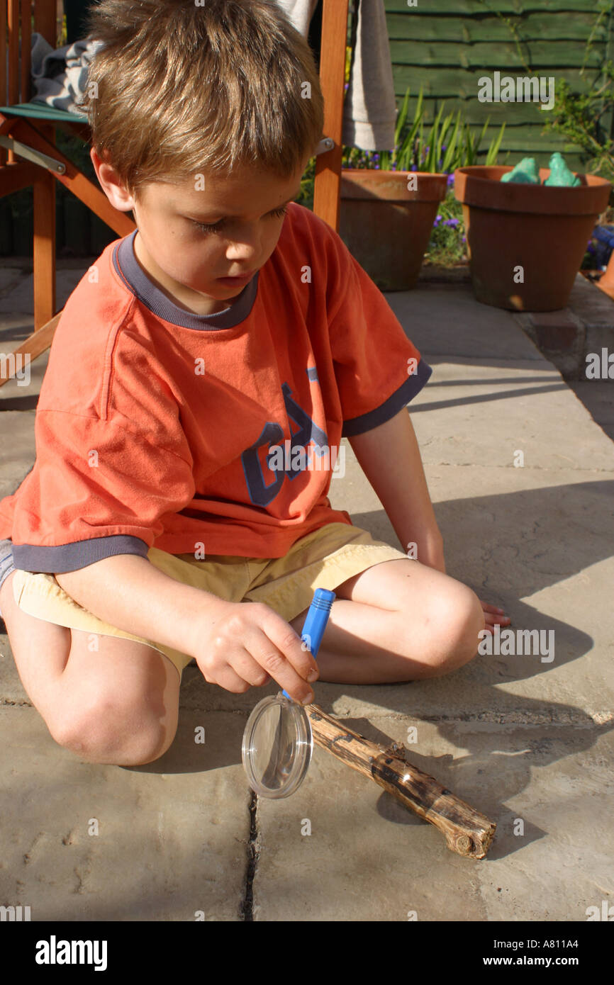 Young boy with magnifying glass focusing suns rays to burn wood Stock Photo