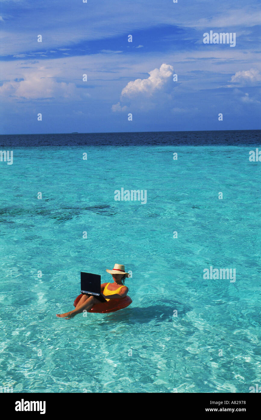 Woman sunbathing on air mattress with laptop computer called an outdoor office Stock Photo