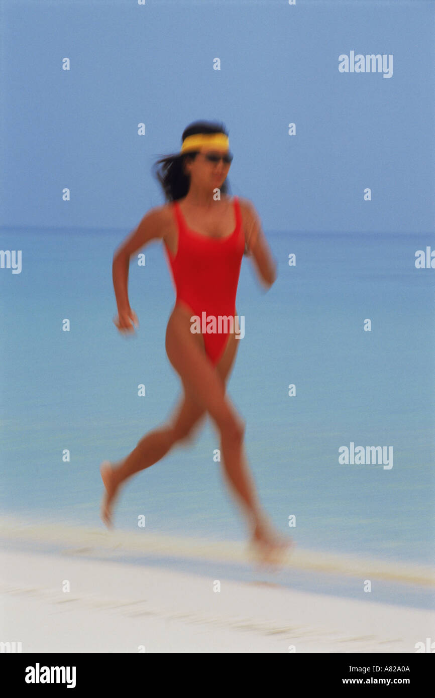 Woman in red swimsuit running along shore Stock Photo