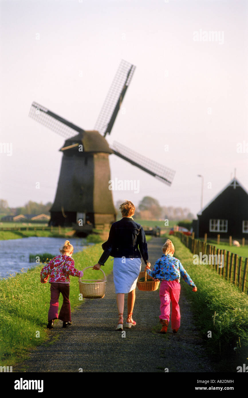 Mother and children with baskets walking home in Holland near windmill and canal Stock Photo