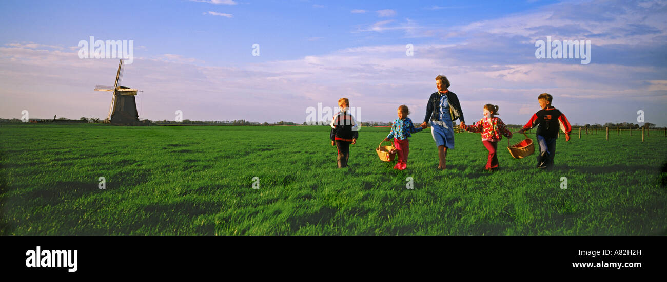 Mother and children with baskets crossing farmlands in Holland near windmill Stock Photo