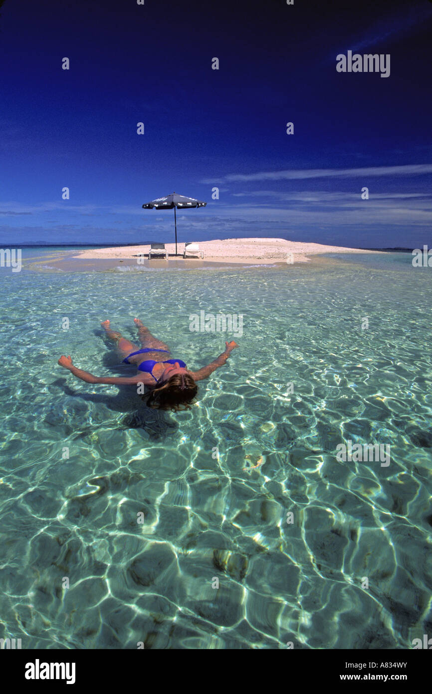 A young girl in bikini floats just off an idylic sand island in Fiji