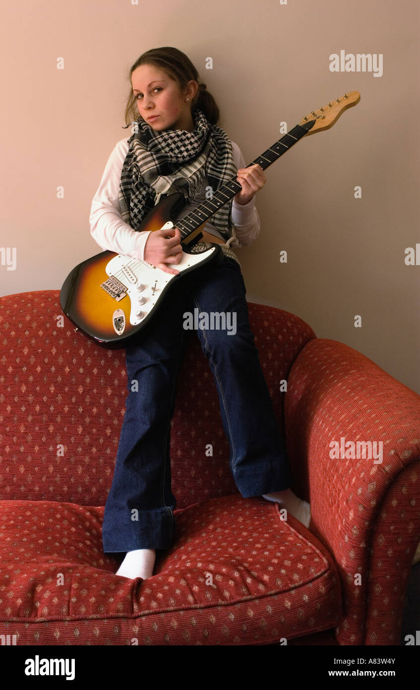 Girl holding an electric guitar sitting on a red sofa Stock Photo