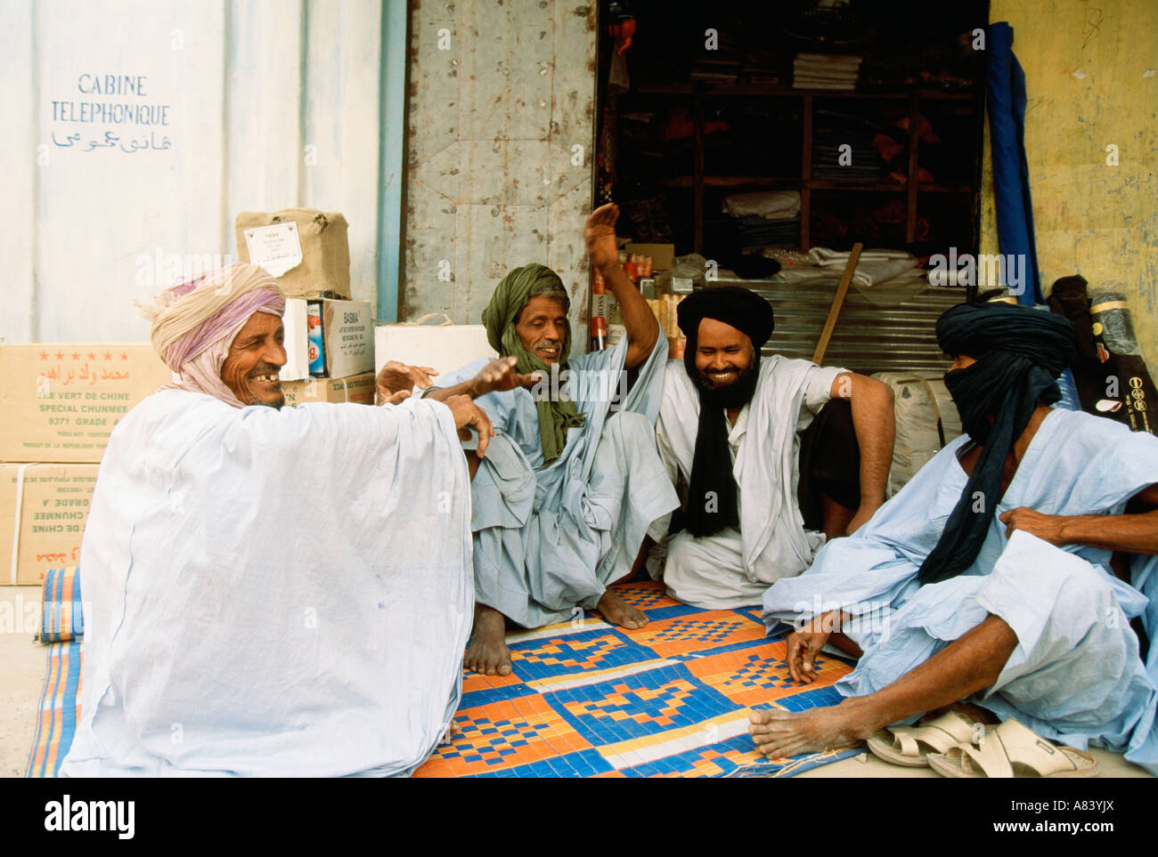 Berber herders in traditional robes sitting outside a shop, talking and laughing Stock Photo