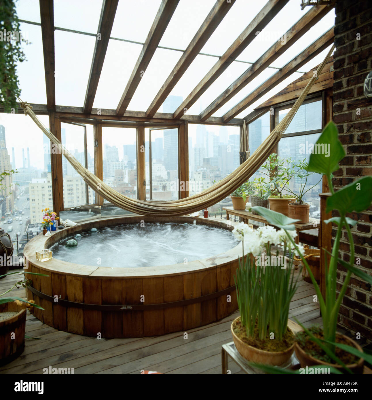 Hammock above hot tub in conservatory bathroom with view of New York through windows Stock Photo