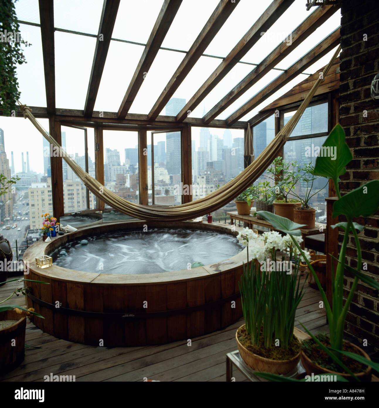 Hammock above hot tub in conservatory extension with view of New York through windows Stock Photo