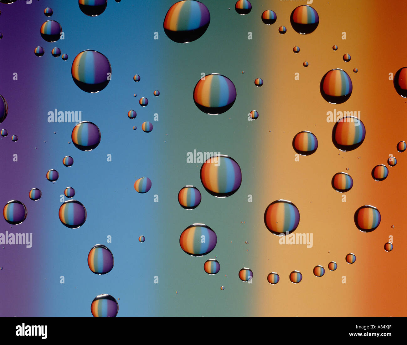 Still life close-up of water droplets on glass surface against backdrop of spectral colours. Stock Photo