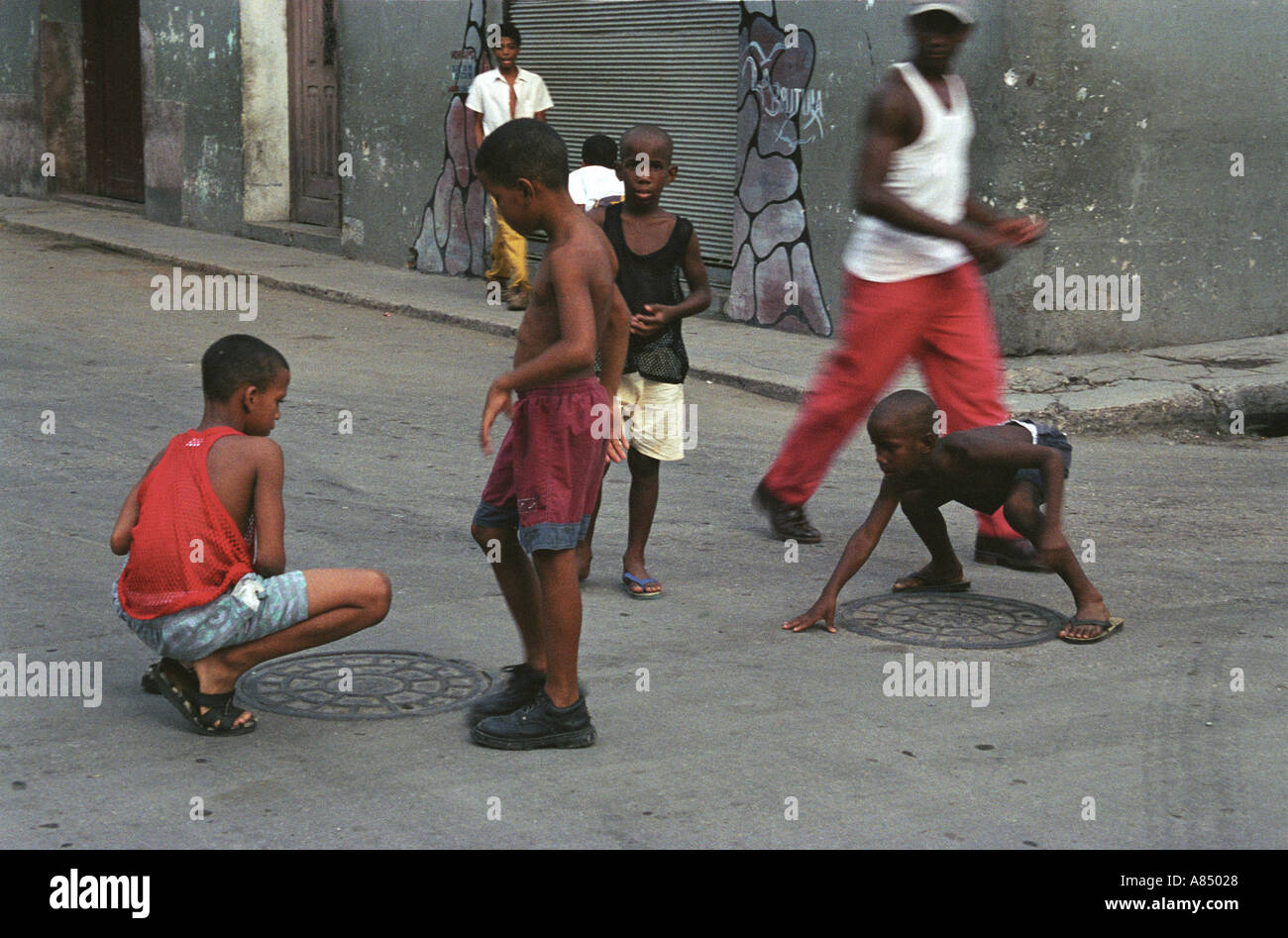Young cuban boys in streets of Central havana participate in game of marbles as pedestrians look on Stock Photo