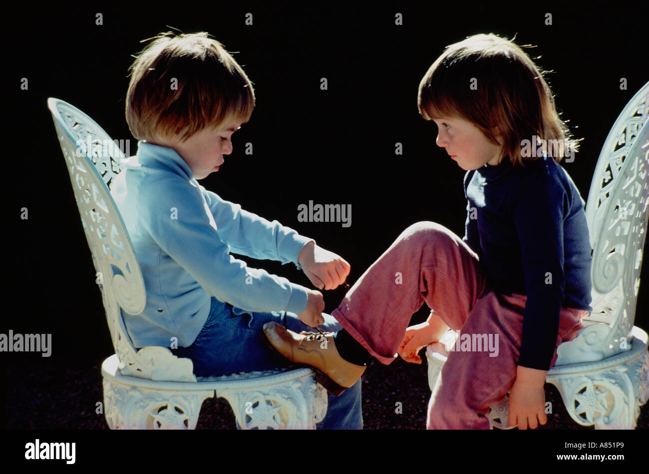 Two boys sitting on garden chairs. Doing up shoe laces. Stock Photo