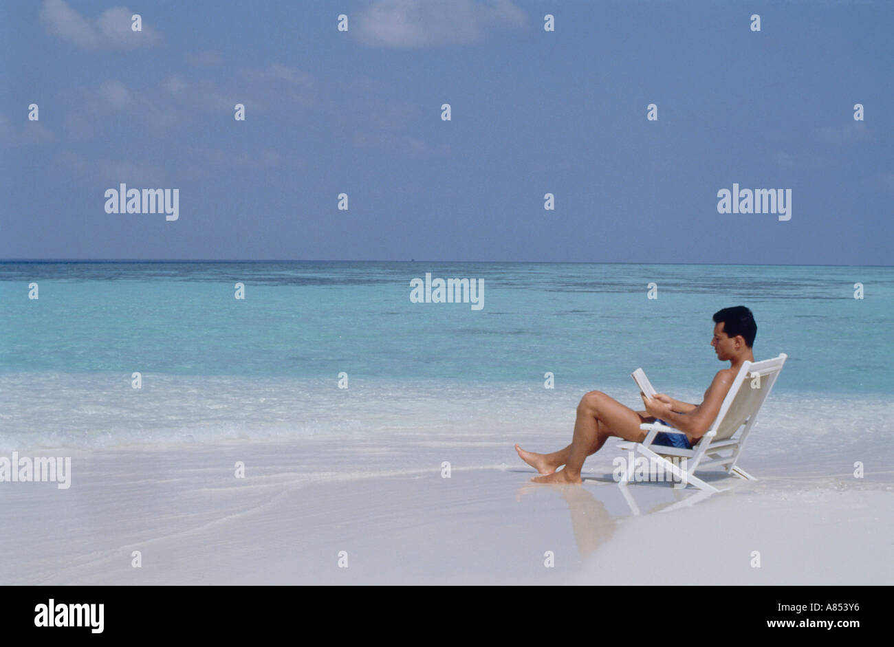 Maldives Young Man In Swimsuit Sitting On Beach Chair In Shallow Water Reading Book Stock Photo Alamy