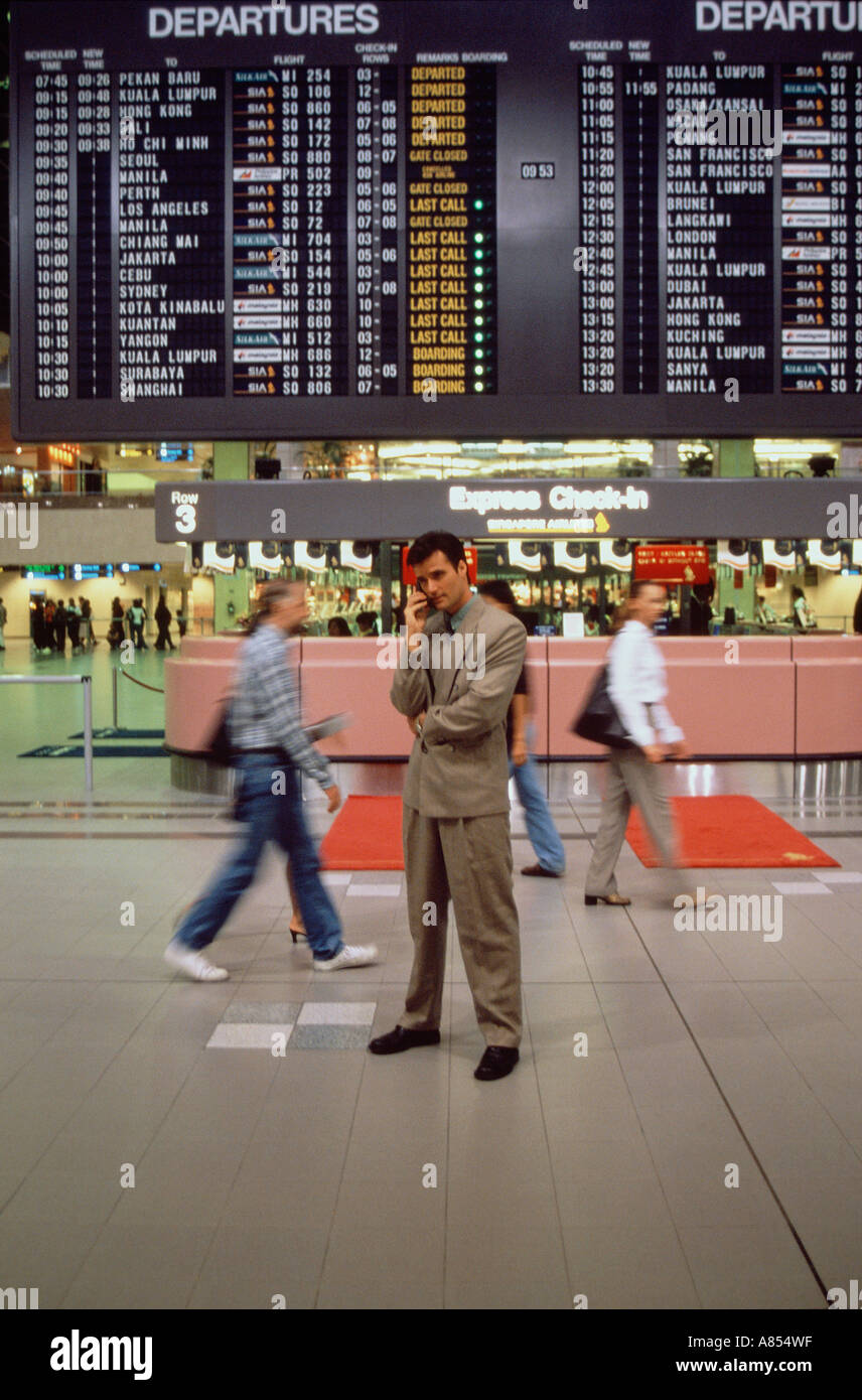 Busy Singapore airport terminal with young man using mobile 'phone. Stock Photo