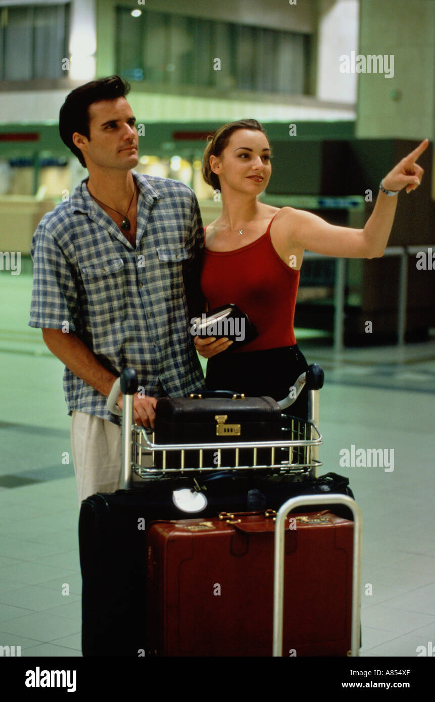 Young couple with luggage trolley at airport. Stock Photo