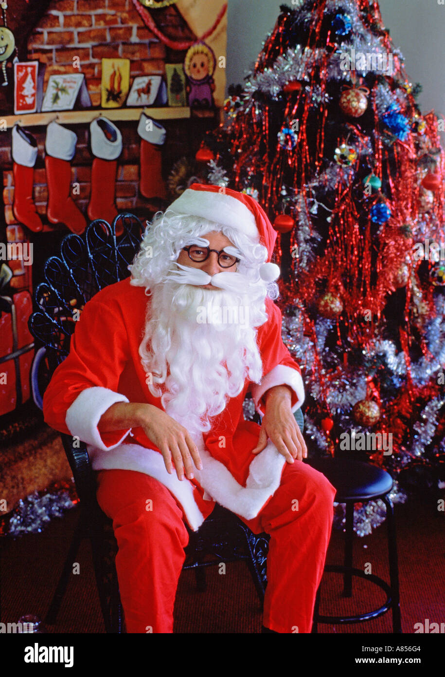 Santa Claus (Father Christmas) sitting in store setting by Christmas tree Stock Photo