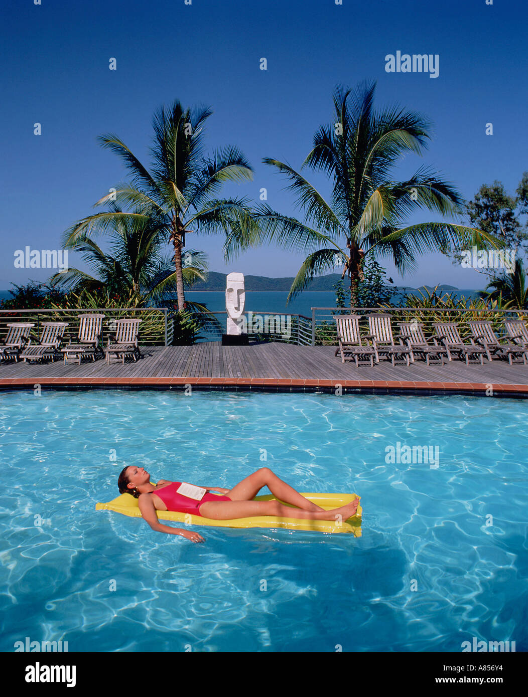 Woman with book on her stomach, reclining on air bed in swimming pool