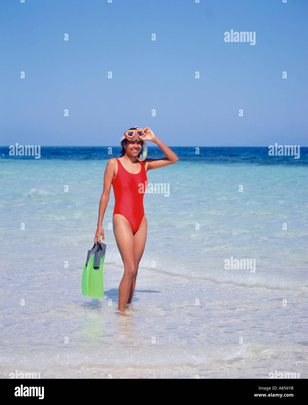 Young woman in swimsuit standing in the water off the beach at Beaver Cay, Great Barrier Reef, Queensland, Australia. Stock Photo