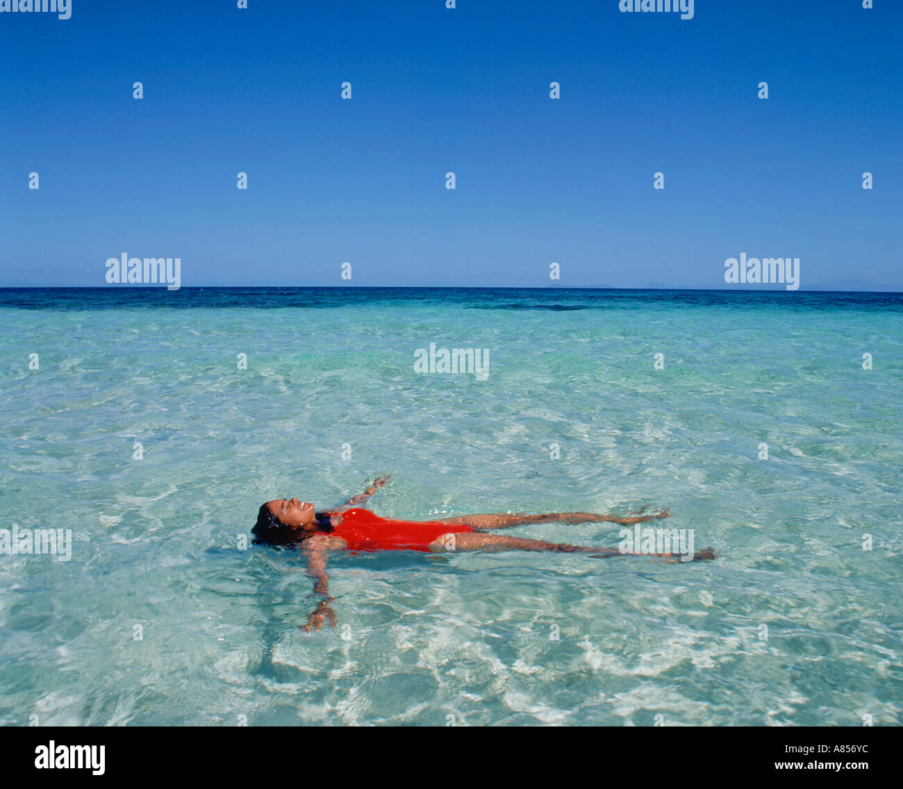 Young woman in swimsuit floating on her back in the water at Beaver Cay, Great Barrier Reef, Queensland, Australia. Stock Photo