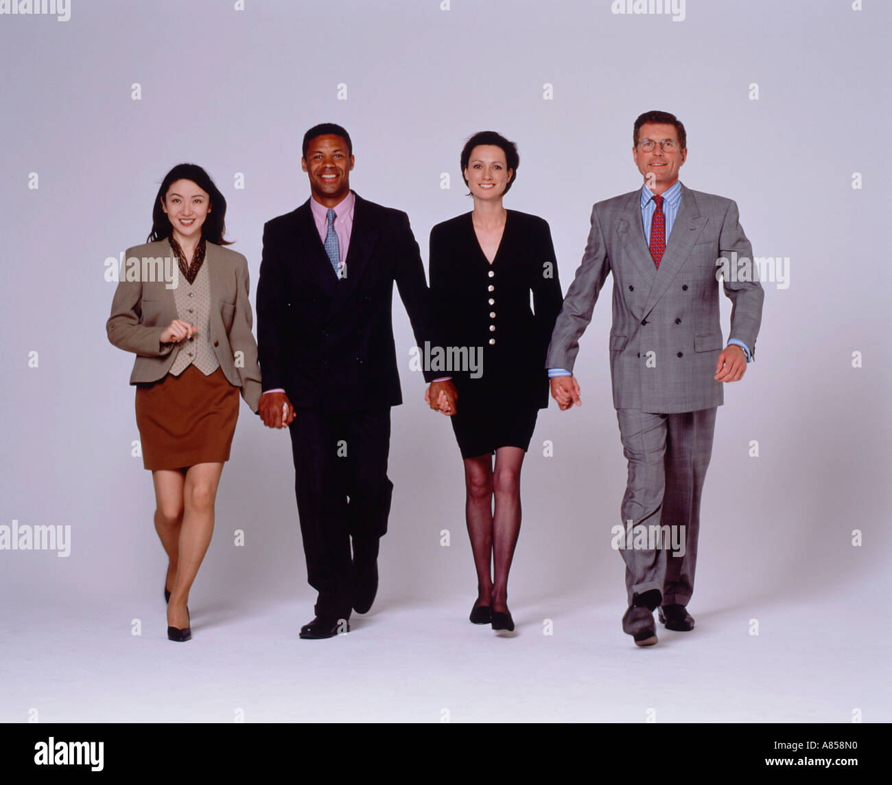 Studio image of a team of four people.  Two men and two women wearing business suits and walking towards camera. Stock Photo