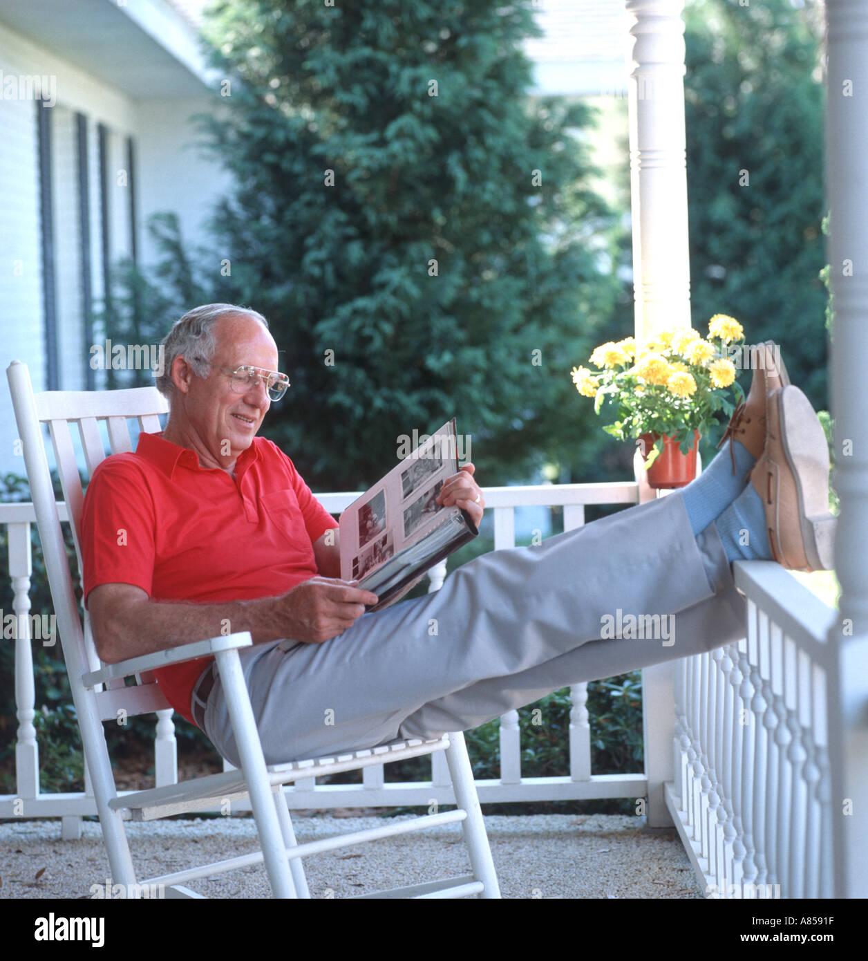 mature man relaxing on rocking chair on wooden porch looking at photo album Stock Photo