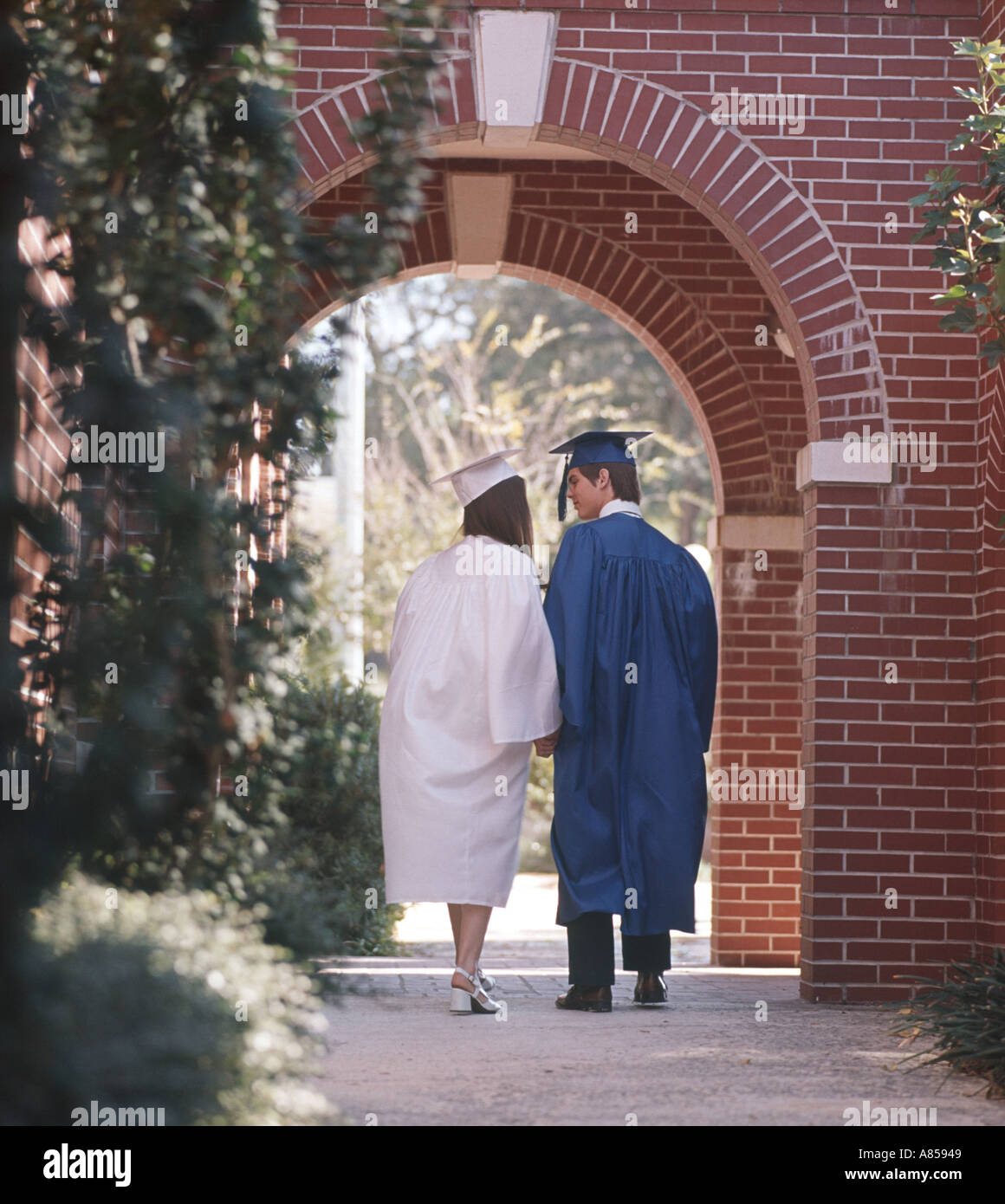 graduation couple in caps and gowns walking through a campus arch Stock Photo