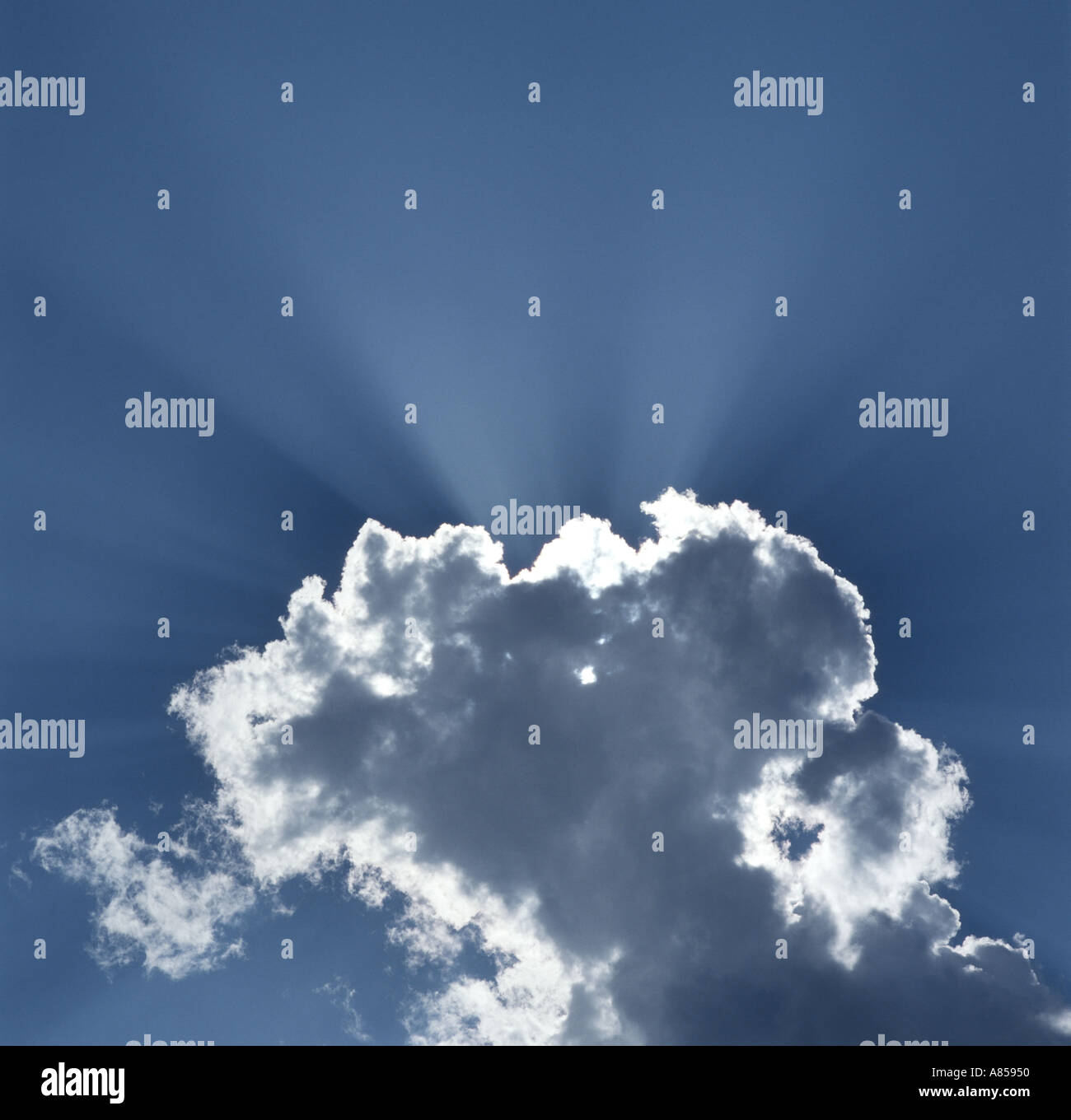 sunburst behind cumulus cloud in blue sky Stock Photo
