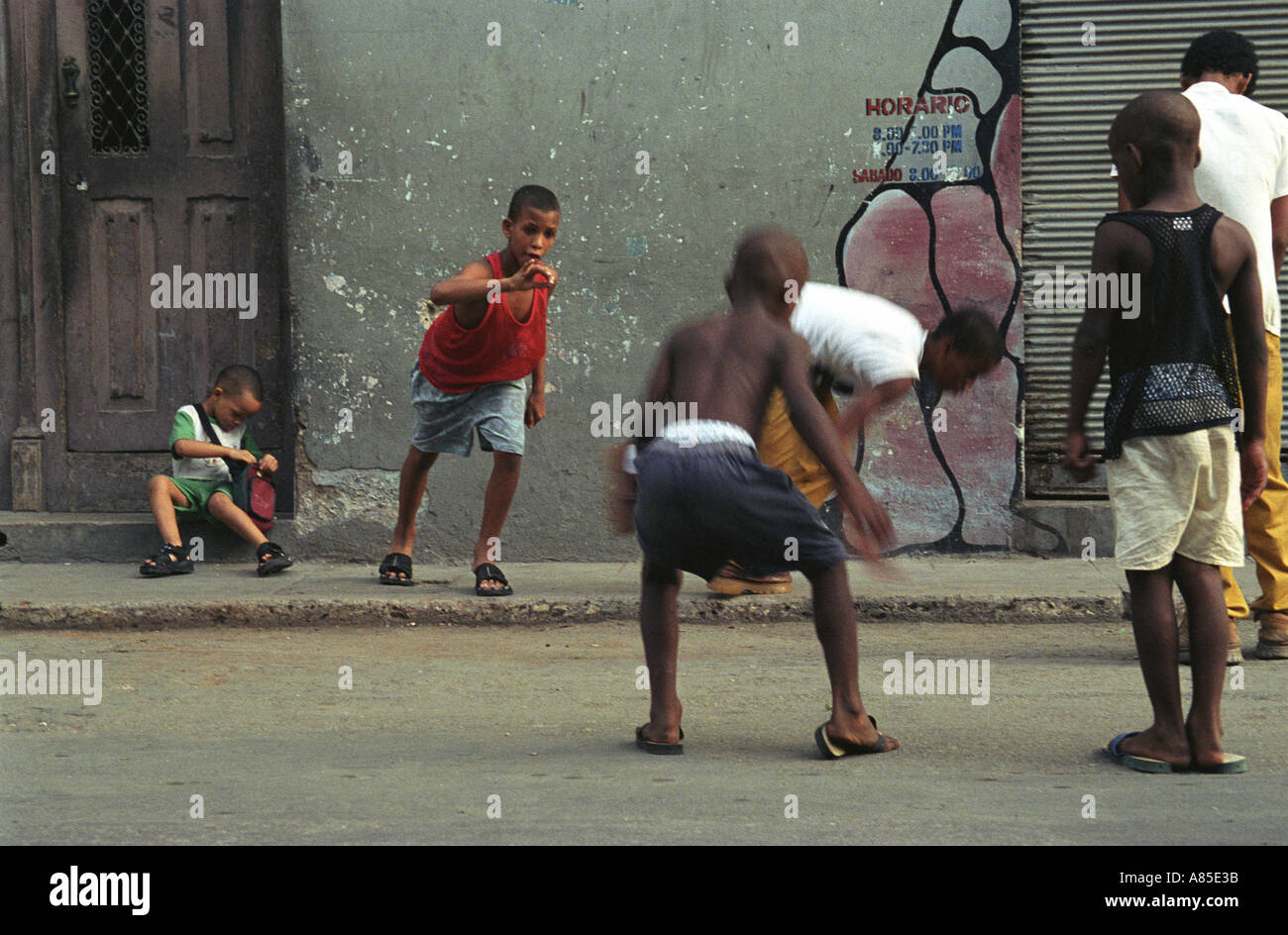 Young cuban boys in streets of Central havana participate in game of marbles as spectators watch seated on doorsteps Stock Photo