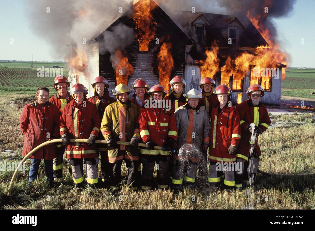 Firefighters pose for a photo while a house burns down Stock Photo