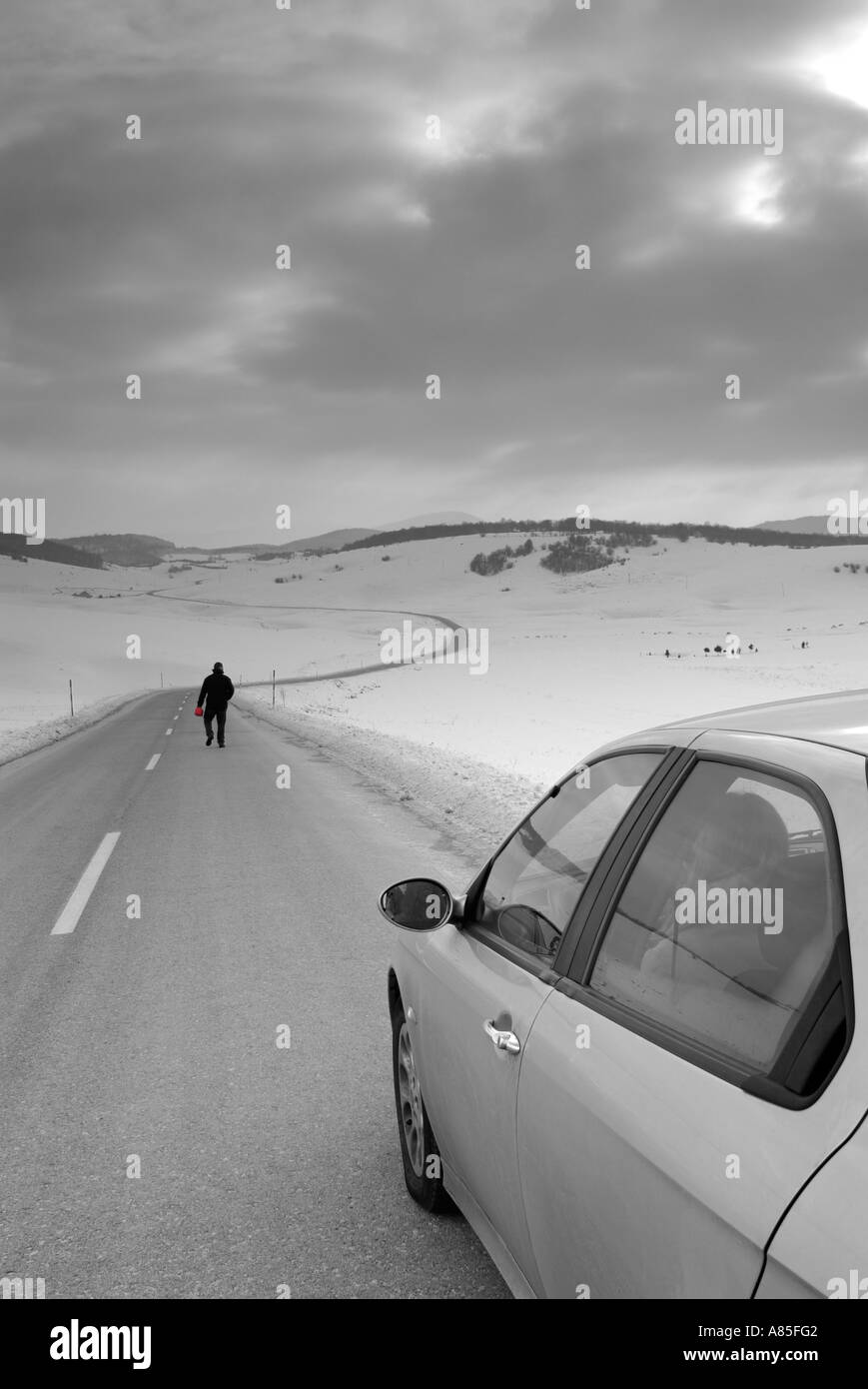 Man leaves his spouse in the car to walk along an isolated road in snow Stock Photo