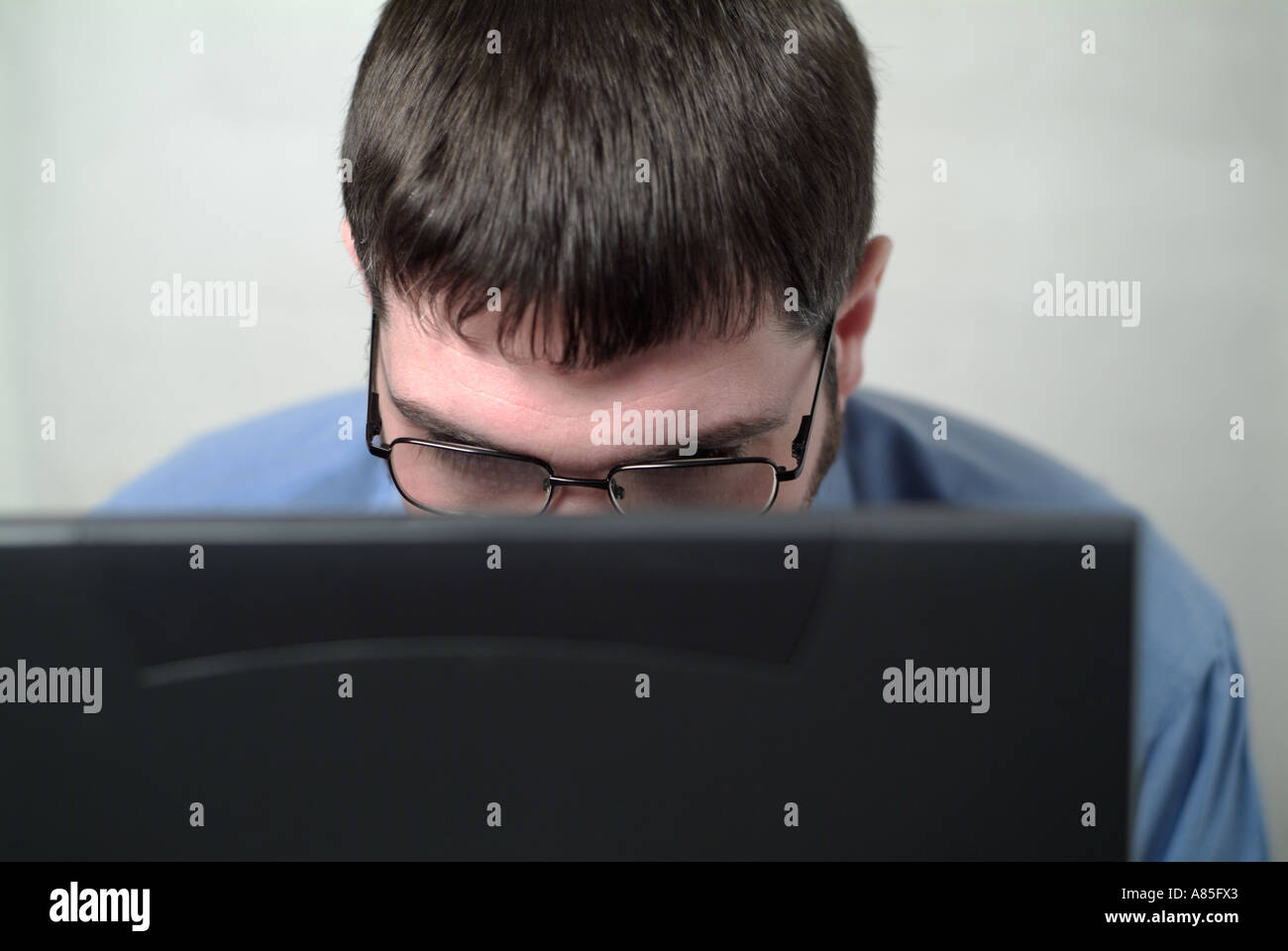Businessman Working On His Laptop Portable Computer With Head And Face Partially Obscured By The Screen Stock Photo