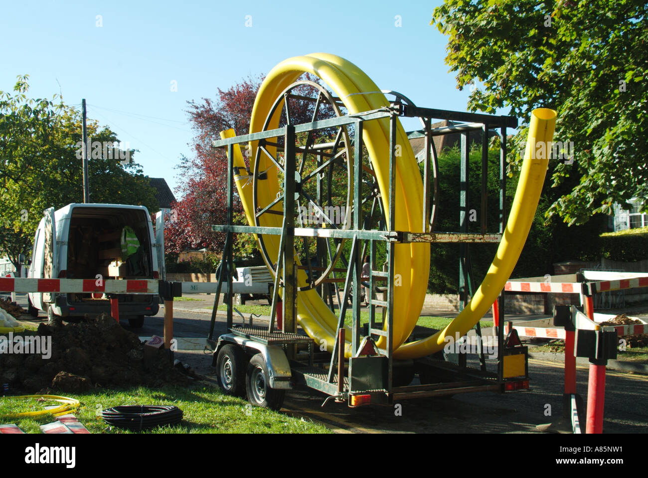 Gas main pipe laying road works in progress with large coil of yellow flexible plastic pipe on trailer Essex England UK with copy space Stock Photo