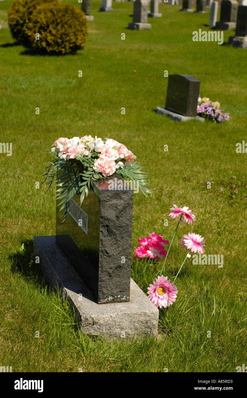 A tombstone with flowers on it in a grass filled cemetery in Canada Stock Photo