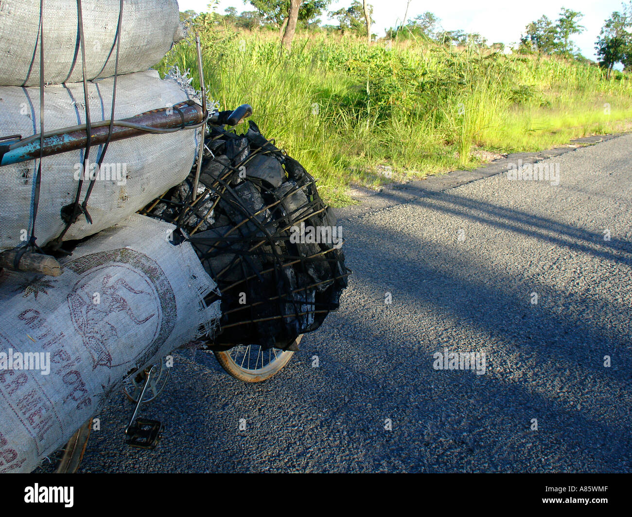 Bike filly loaded with charcoal bags on side of empty asphalt road being carried to Lusaka in Zambia, contributing to deforestation problem Stock Photo