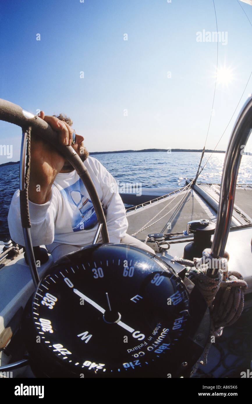 Man at helm of sailboat with hand on wheel and showing compass heading Stock Photo