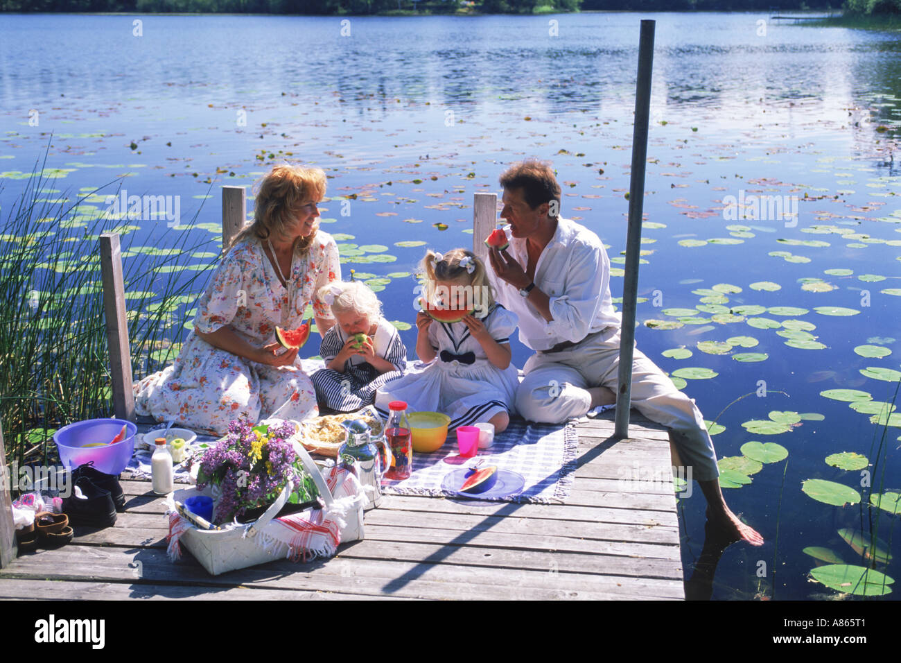 Family of four with picnic basket on lakeside pier during Swedish