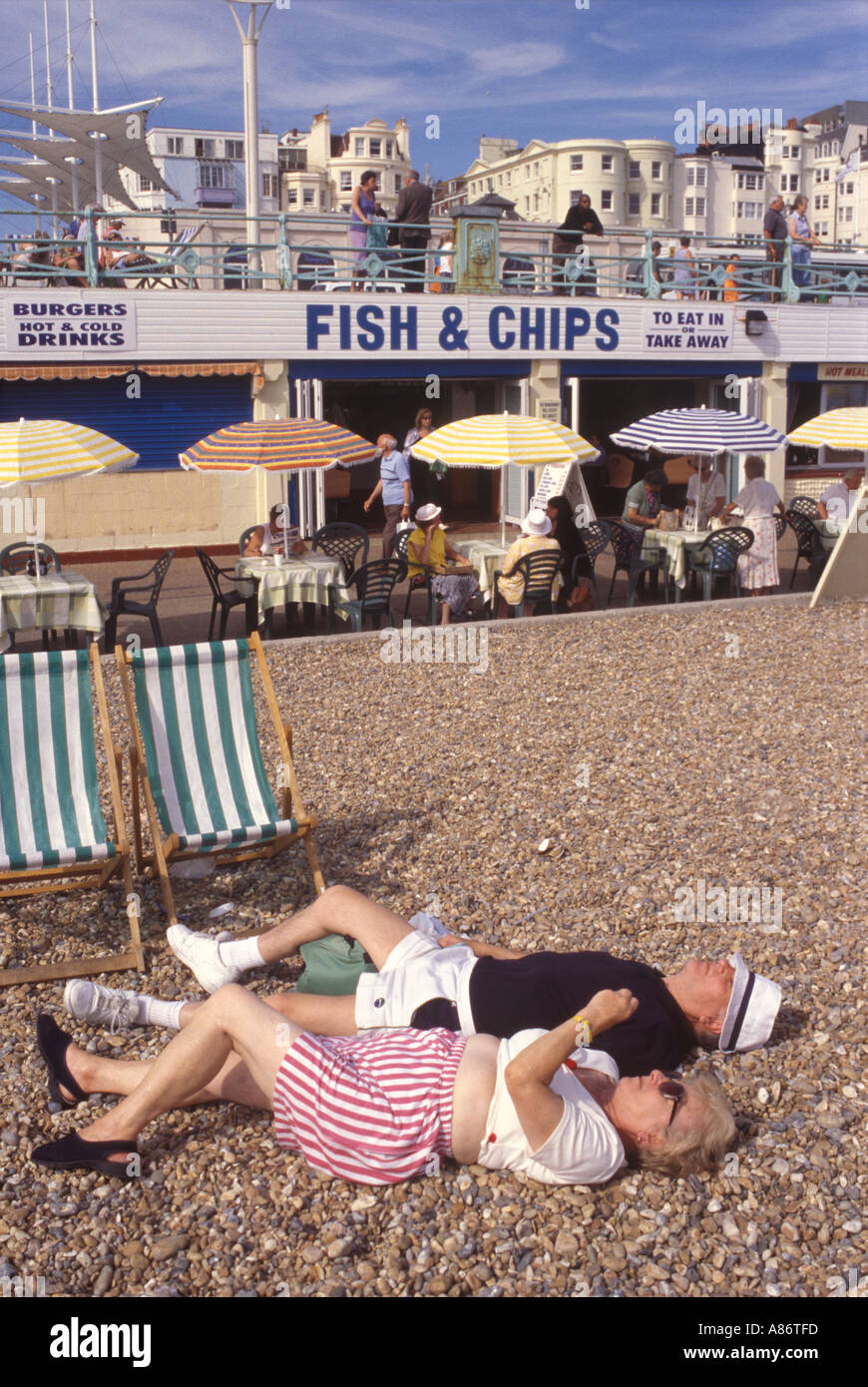 Brighton Seafront An elderly couple enjoy summer sunshine lying on the pebble beach Sussex HOMER SYKES Stock Photo