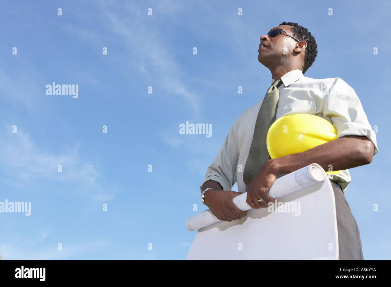 man rolling up plans, his hard hat under his arm in the open air Stock