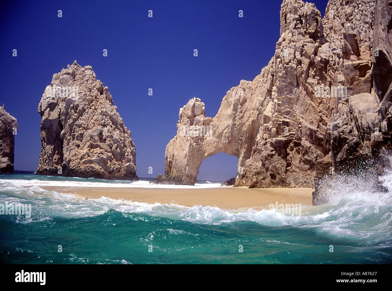 Tropical waters spilling on to an isolated beach with an arch in a rock formation carved by the sea Stock Photo