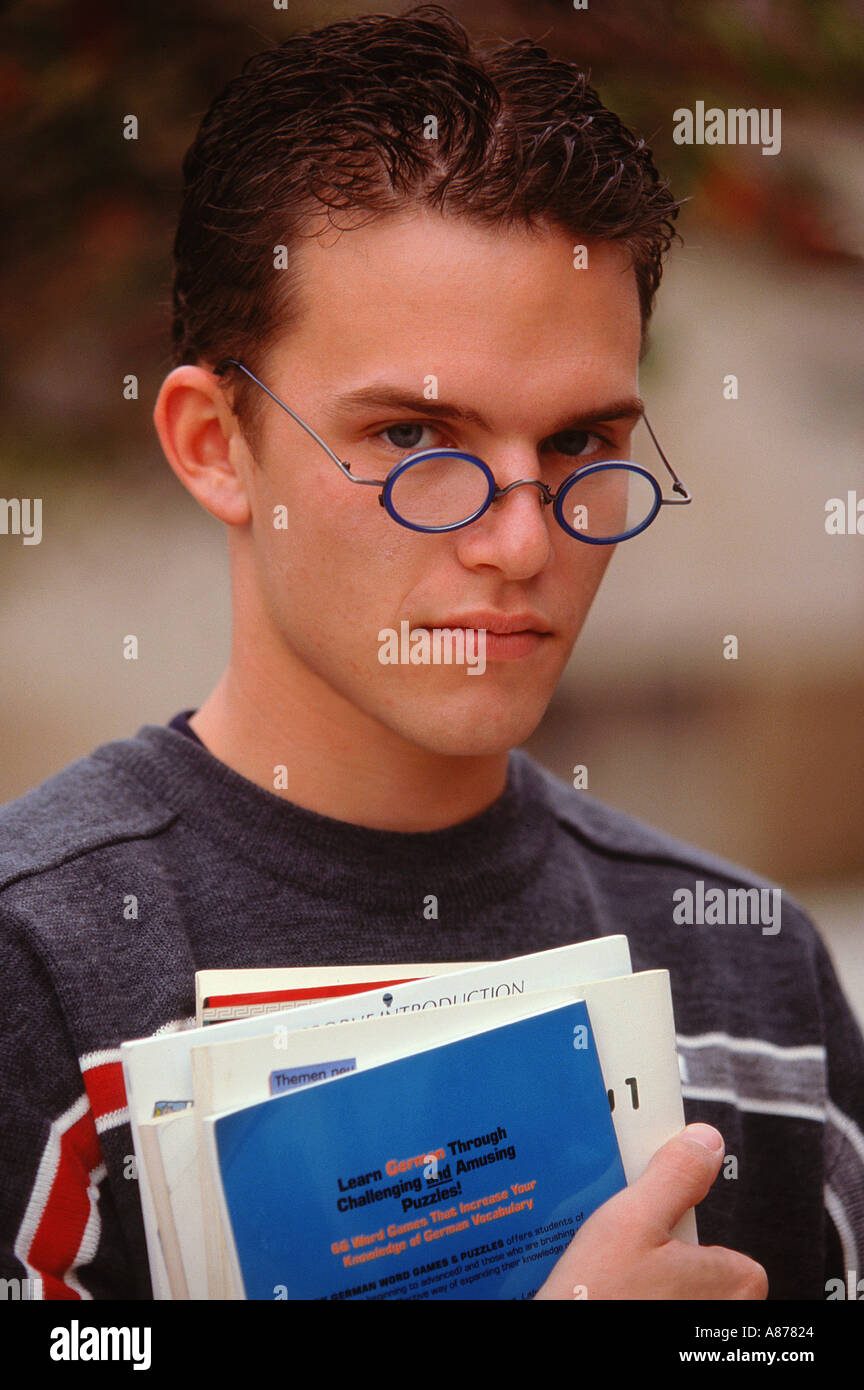 A brown haired male teenager wearing blue rim glasses low on his nose a sweater carrying books outdoors  Stock Photo