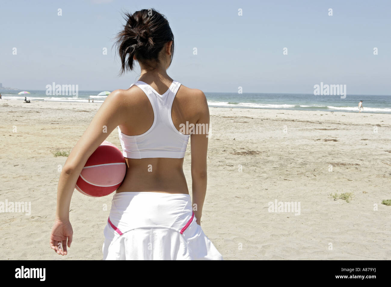 A woman is holding a rubber ball and standing on a beach. Stock Photo