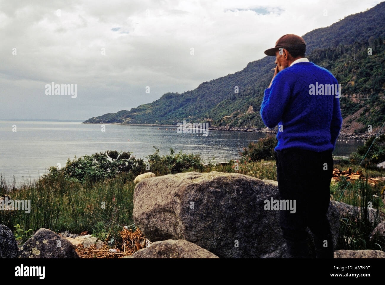 Old fisherman smoking a cigarette and looking out to sea in La Arena Patagonia Chile Stock Photo