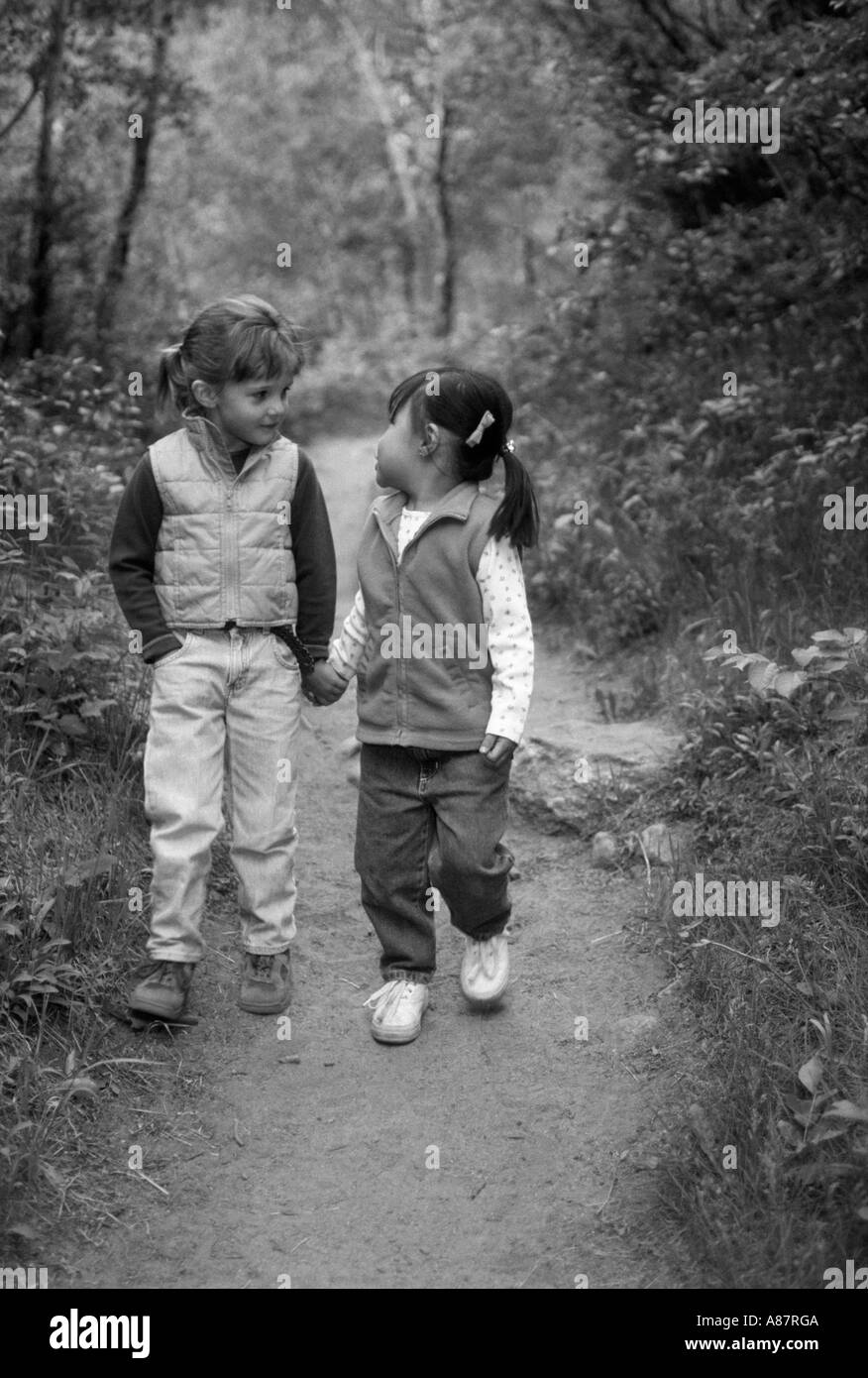 Black and white image of two young girls holding hands while walking down a forest trail in the Rocky Mountains Stock Photo