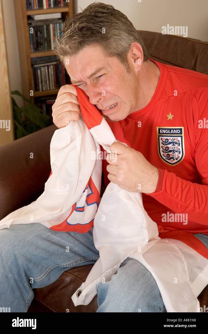 England football fan sitting at home on sofa in front of TV crying into his St. George's flag as his team has just lost. Stock Photo