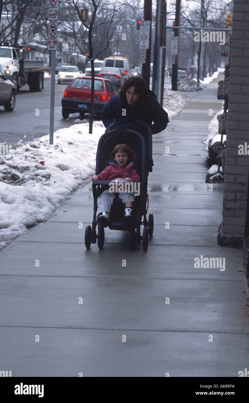 Woman pushing youngster in stroller Stock Photo