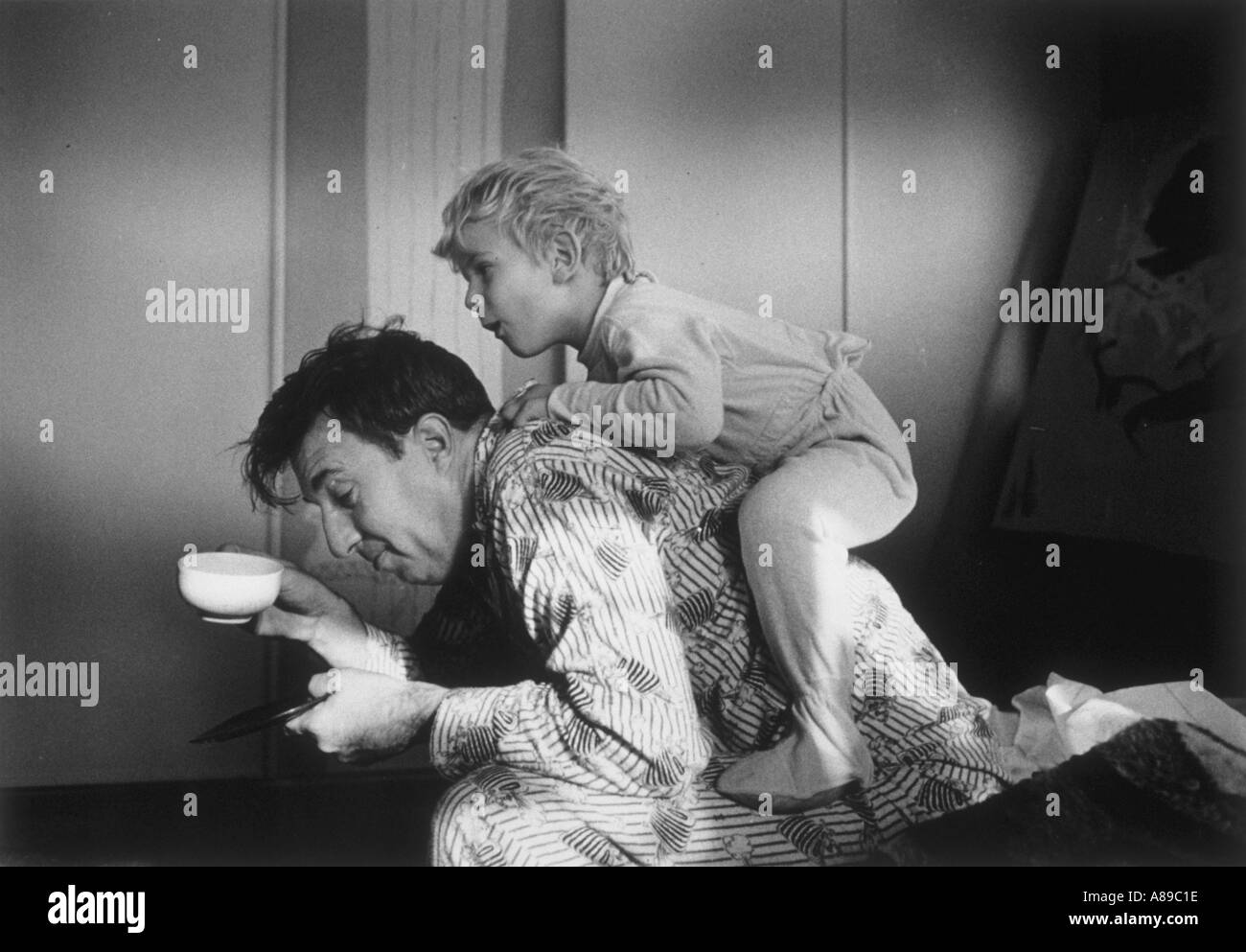 Eager young son jumps on his father back while his father tries to drink a cup of coffee in the morning Stock Photo