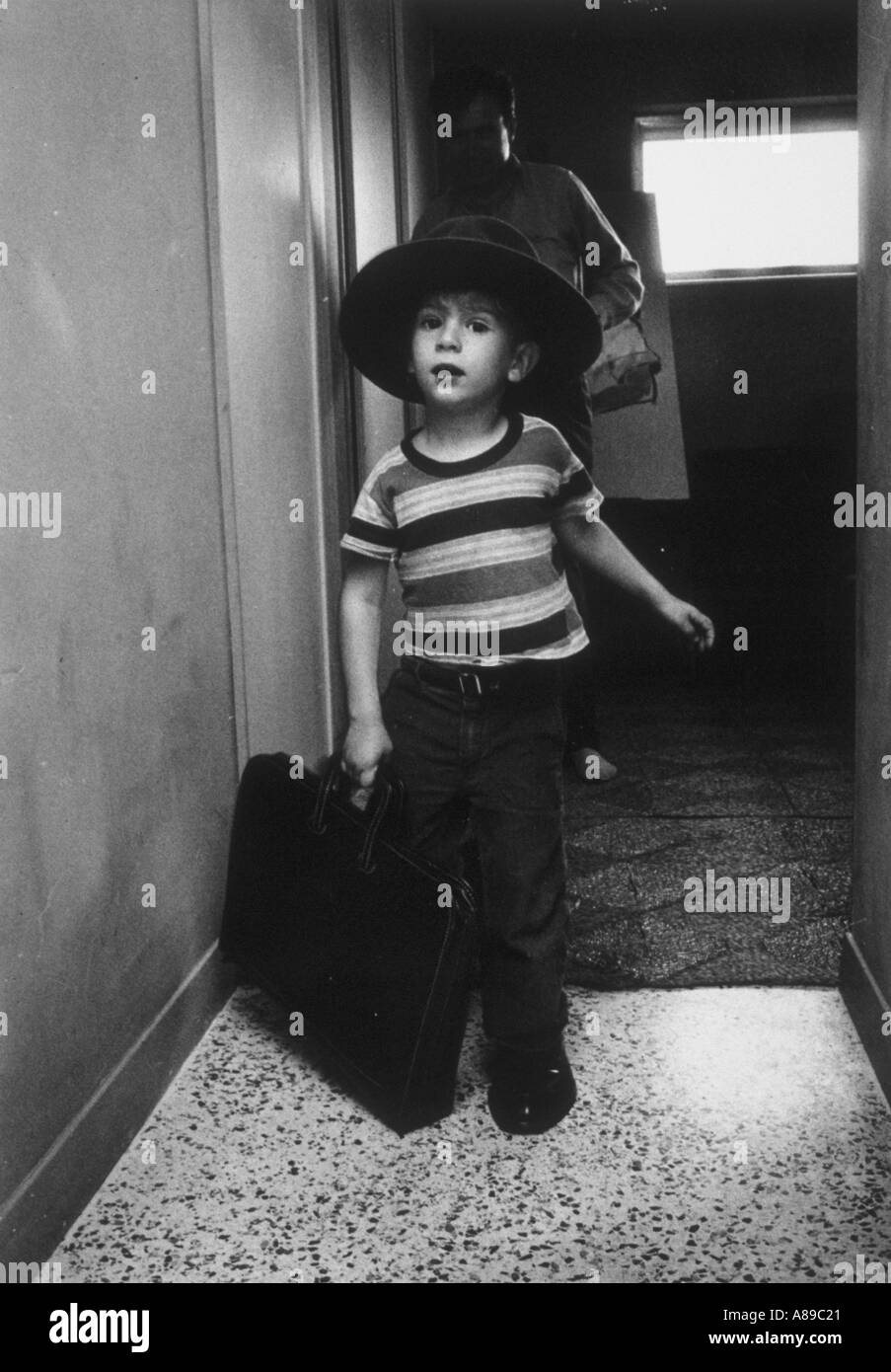 Young boy emulates his father by wearing his father hat and shoes and carries his briefcase Stock Photo