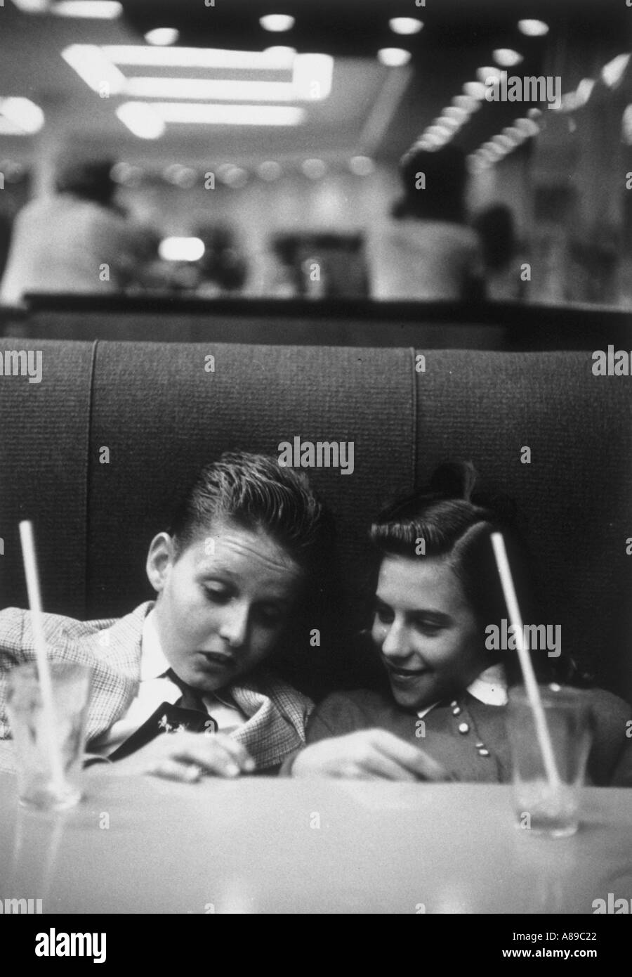 Teenage boy and girl sitting in a booth at a 1950 drugstore sharing soda on a date Stock Photo