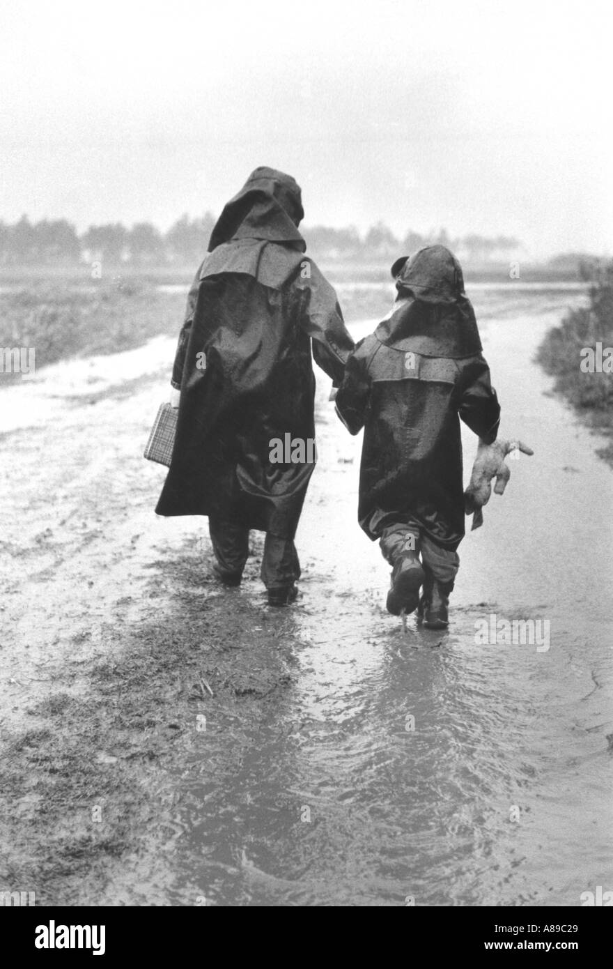 Two children in rain hats and raincoats walking in the rain Stock Photo