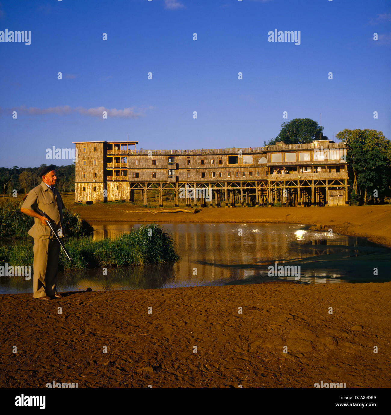 A local warden with rifle standing by the animals waterhole at the famous Treetops safari lodge in Kenya East Africa Stock Photo