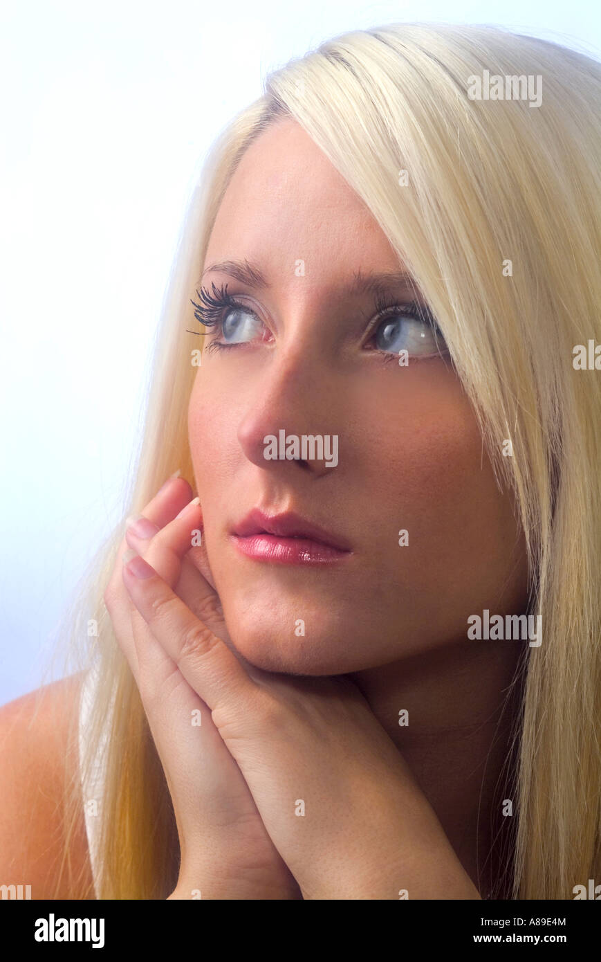 Close up of a pretty young woman with long blond hair looking serious with hands under chin Stock Photo