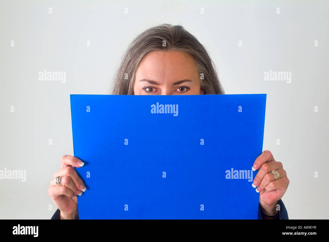 View of a mature woman holding a blank blue sign in front of her face ...