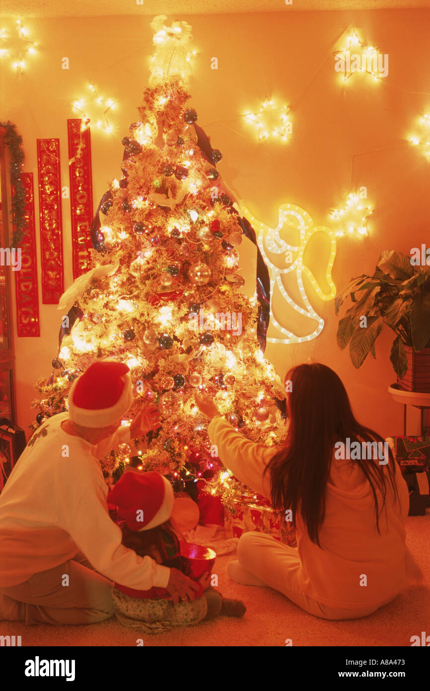 Family of three generations sitting under brightly lit Christmas tree Stock Photo